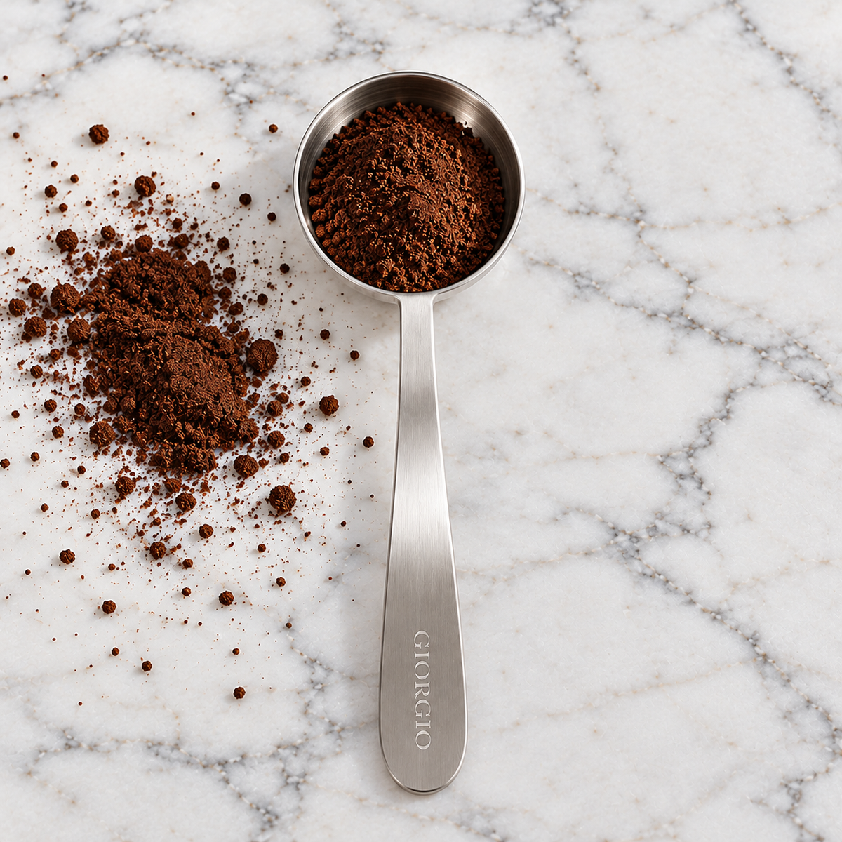 Giorgio stainless steel coffee scoop filled with ground coffee on white marble