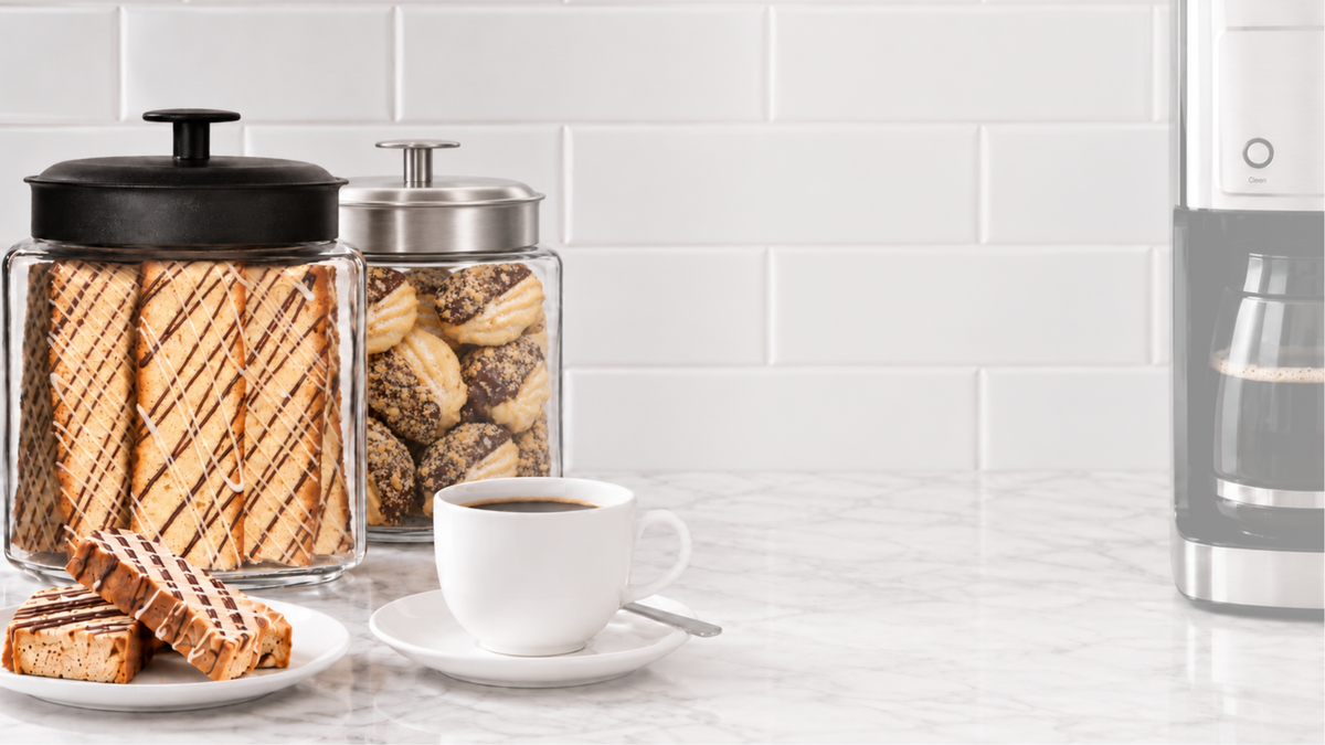 Giorgio signature biscotti jar with a black lid beside a cookie jar with a brushed nickel lid on a marble counter