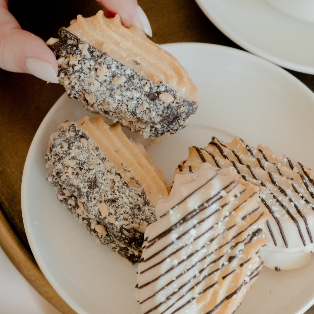 A hand lifting a chocolate-dipped hazelnut cookie from a white plate