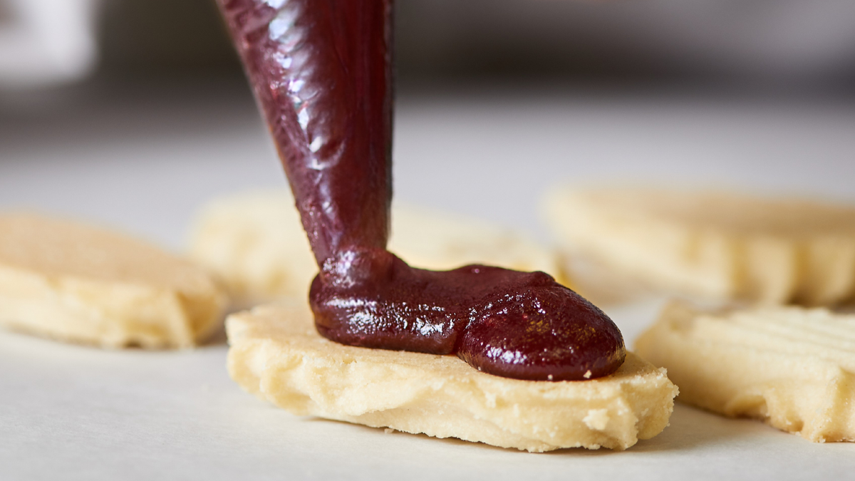Raspberry filling being hand-piped onto a shortbread cookie